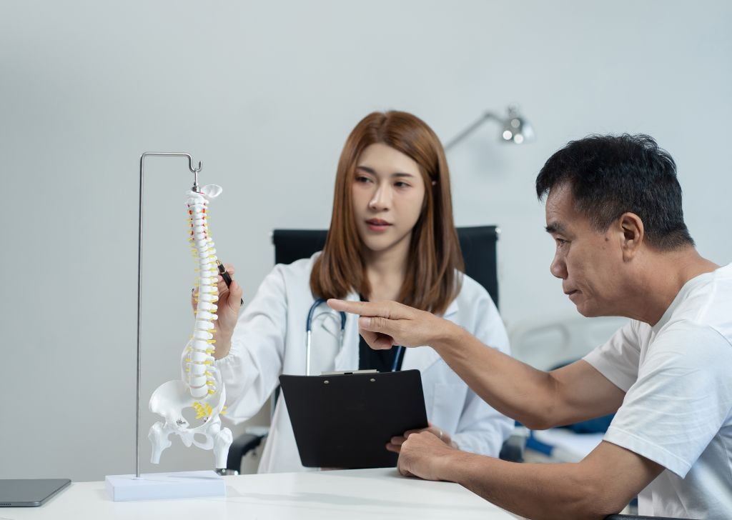 A chiropractor explains the problem to a patient using a spine model.
