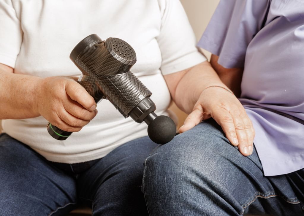 A chiropractor applying percussive therapy with a massage gun.