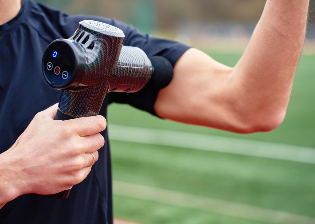 An athlete using a massage gun for percussive therapy.