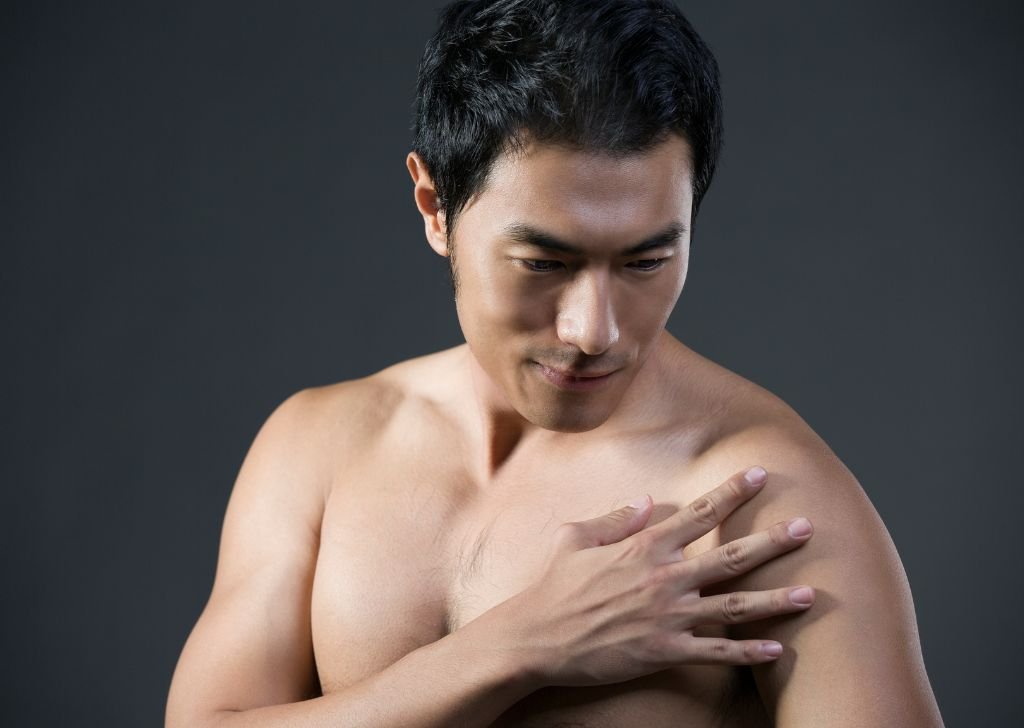 An Asian bodybuilder having muscle pain that requires percussive therapy.