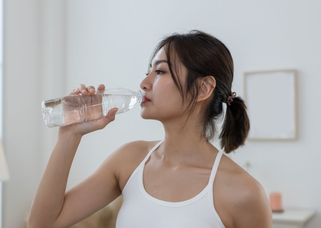 A woman drinking water to stay hydrated. Proper hydration prevents leg cramps. 
